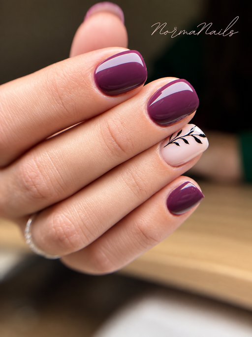 Ongles courts arrondis, prune brillant avec un ongle d'accent rose pâle orné d'une fine branche de feuillage noire.