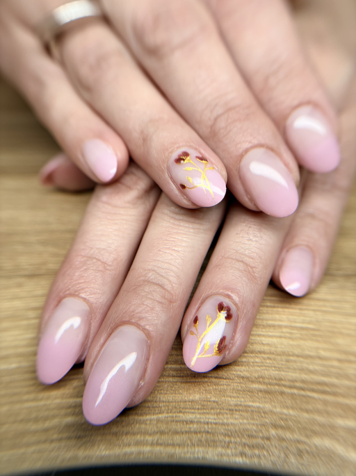 Ongles amande de longueur moyenne, rose poudré fondu vers le blanc, deux ongles ornés de feuille d’or et de petites touches bordeaux.