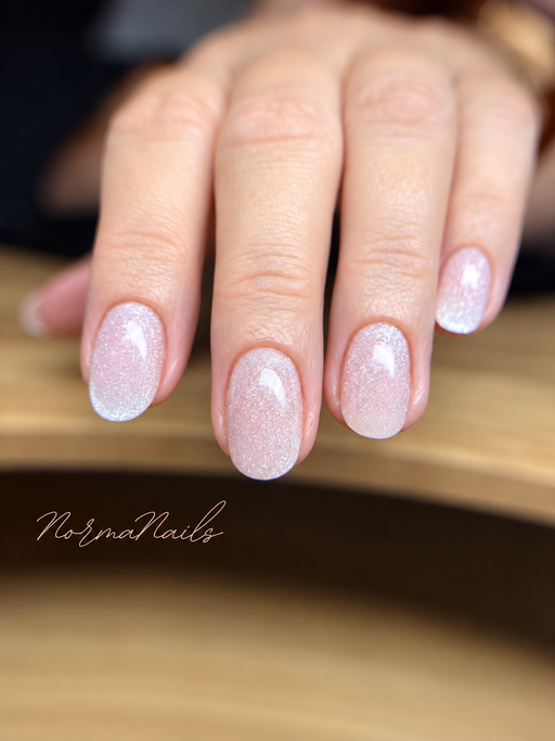 Ongles courts arrondis, rose pâle pailleté aux reflets irisés, finition brillante.