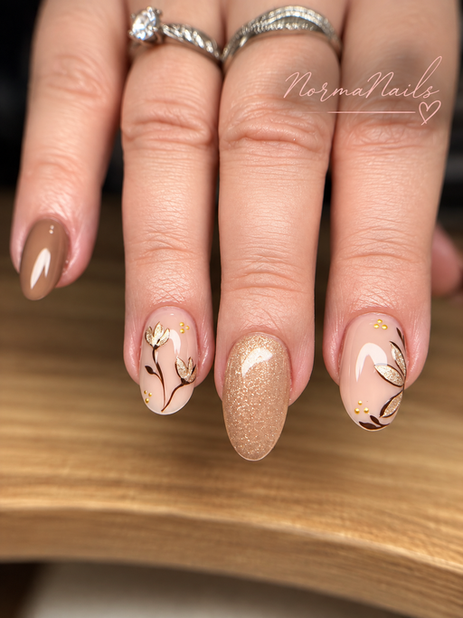 Ongles amande de longueur moyenne alternant taupe brillant, champagne pailleté et nude orné de fleurs et de feuilles dorées peintes à la main.
