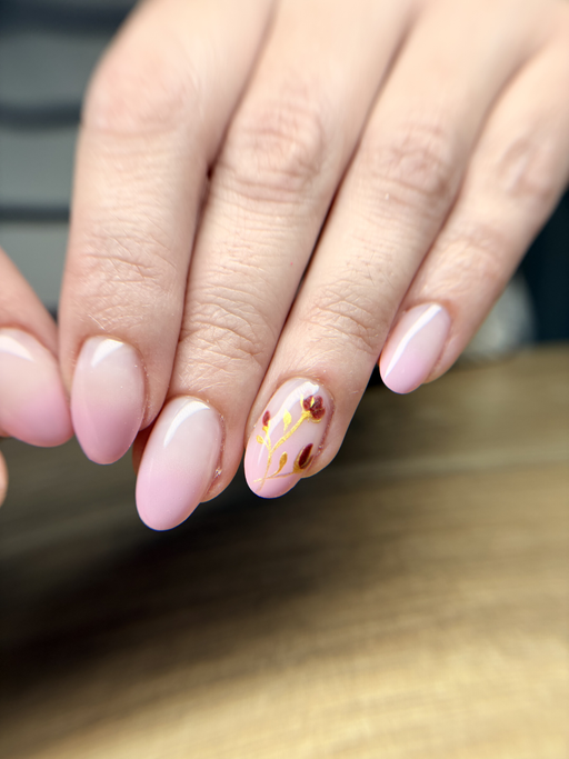 Gros plan sur des ongles amande de longueur moyenne, rose poudré fondu vers le blanc, un ongle orné de feuille d’or et de touches bordeaux.