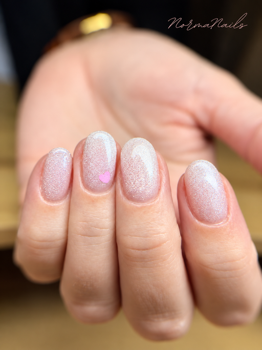 Ongles ovales courts, rose pâle pailleté aux reflets irisés, un ongle orné d’un petit cœur rose.