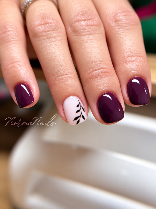 Ongles carrés courts, prune brillant, un ongle rose pâle orné d’une fine branche de feuillage noir.
