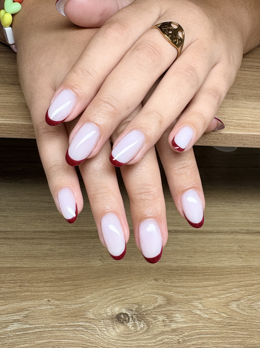 Ongles amande longs, rose laiteux avec une French bordeaux fine et brillante, les deux mains posées l’une sur l’autre.