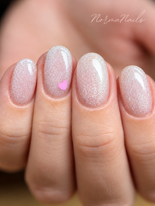Ongles courts arrondis, rose pâle à paillettes argentées, un ongle orné d'un petit cœur rose.