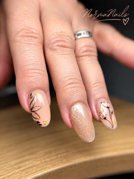 Ongles amande de longueur moyenne, nude rosé, un ongle pailleté champagne et deux ongles ornés de fleurs et de feuillages dessinés en noir et doré.